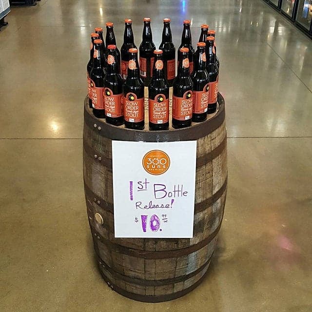 Display of Slow Order Stout bottles arranged on a wooden barrel with a sign announcing 300 Suns Brewing’s first bottle release.