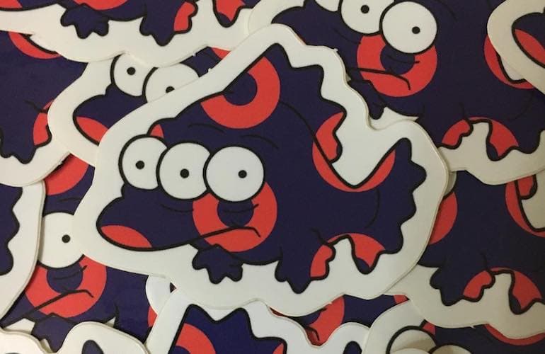 A group of die cut stickers featuring a cartoon three eyed fish character in dark purple with red donut shaped markings.