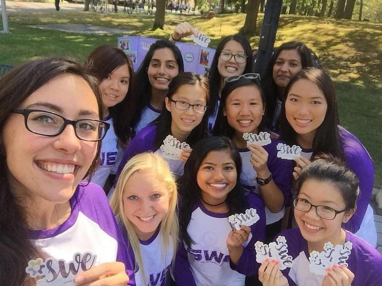Group of students wearing matching SWE shirts holding custom SWE stickers while posing for a group photo outdoors.