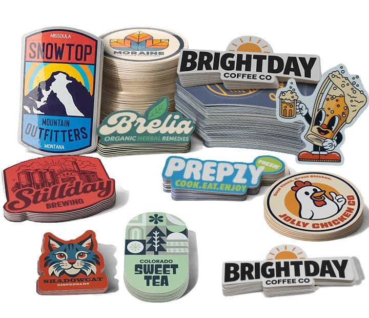 Assorted custom die cut logo stickers in various shapes and designs, stacked and displayed for different brands including coffee, brewing, outdoor, and food businesses