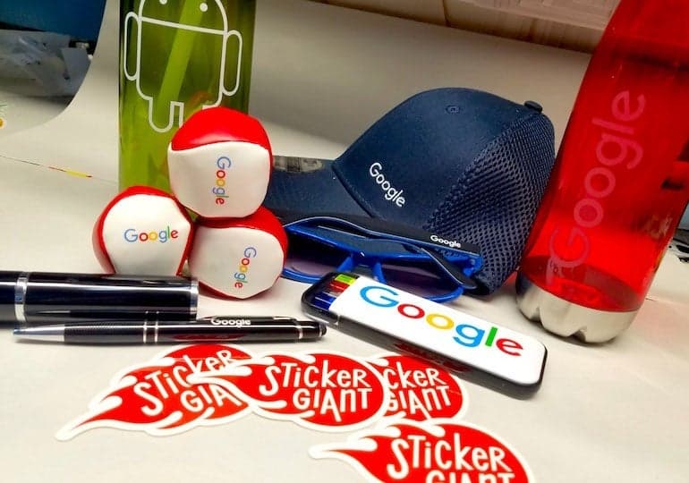 Assorted Google branded swag items displayed on a table alongside several StickerGiant logo stickers.