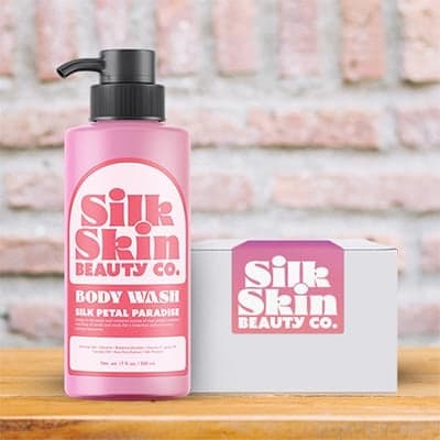 Pink Silk Skin Beauty Co. body wash bottle with a custom product label, displayed next to branded packaging box on a wooden surface
