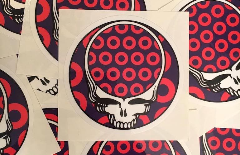 A circular sticker design featuring a stylized white skull with an open top, filled by a pattern of red donut shaped circles on a dark purple background.