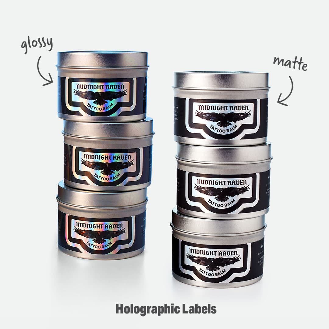Side-by-side comparison of glossy vs matte finishes on custom holographic labels, featuring Midnight Raven Tattoo Balm tins.