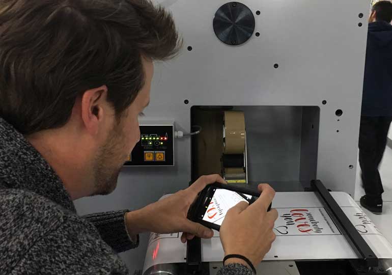 Person taking a close up photo of printed stickers on a production machine.